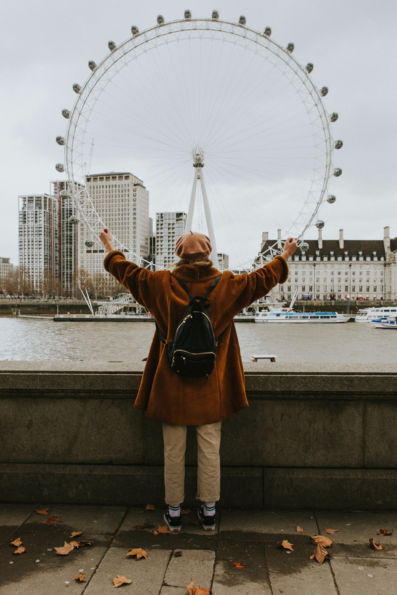 Woman in front of London Eye with autumn foliage